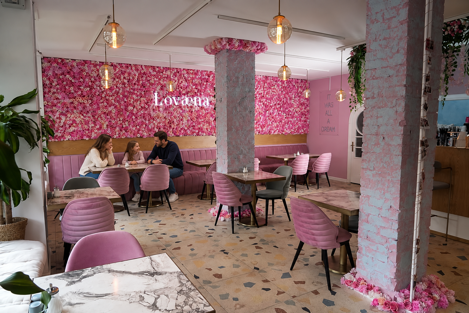 Blog 11 blog Eine Familie sitzt an einem Tisch im Lovaena Café mit rosa Sitzmöbeln und blumengeschmückter Wand.
